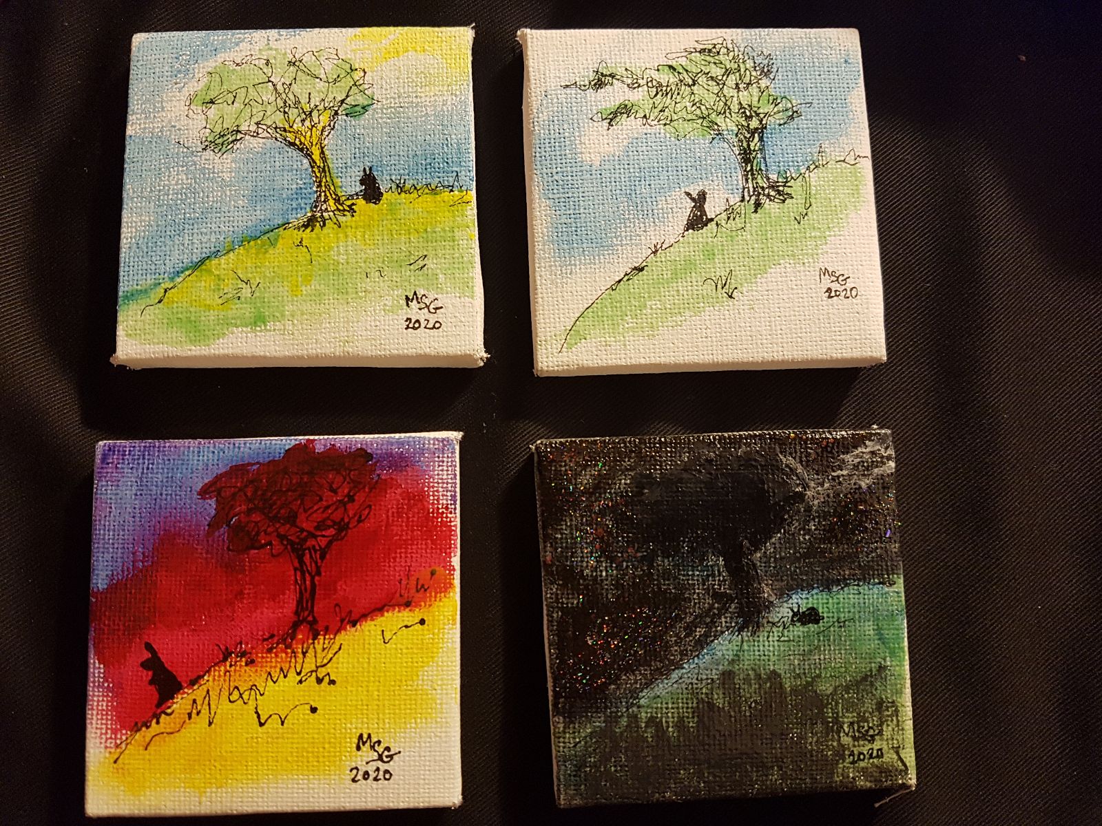 Four small paintings of a rabbit on a hillside next to a tree. Each is pictured at a different time of day: One in golden dawn light, one in midday sun, one at sunset, one at night, with glittering stars.