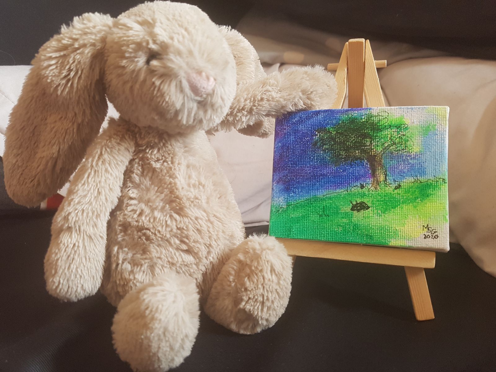 Tiny Bunny is posed as the artist of another small rabbit painting on an easel, this one with a deeper blue sky and two smaller rabbits munch on grass alongside the original bunny.