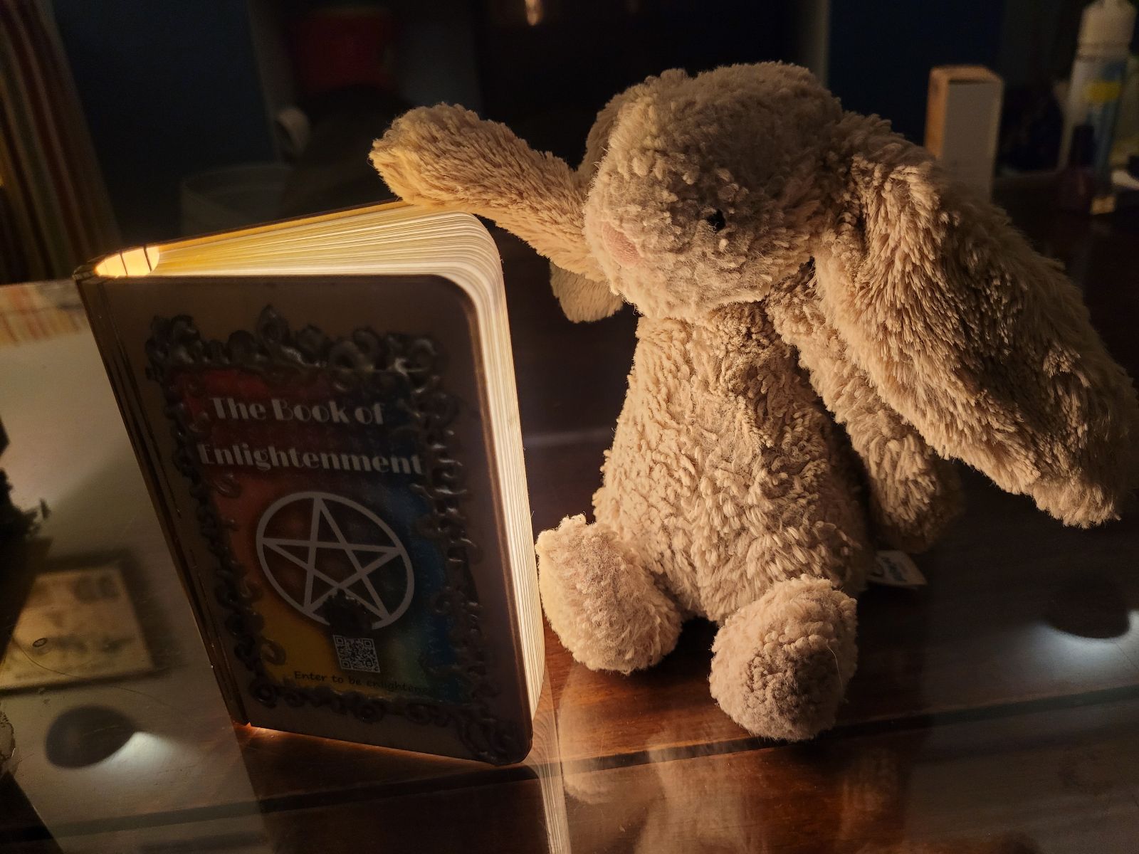 A toy rabbit is posed with his hand on the open book. His face is lit up by the light coming from inside.