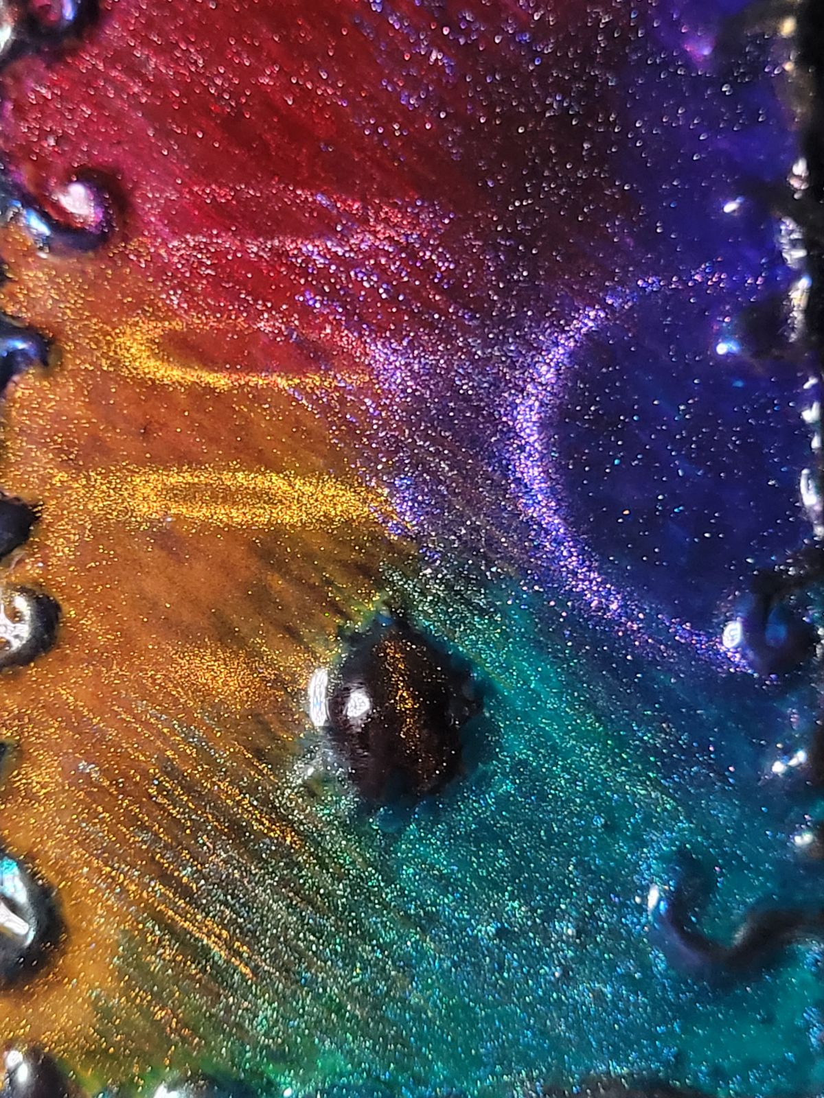 Closeup of a multicoloured field of metallic resin, with circular patterns caused by magnets acting from underneath.