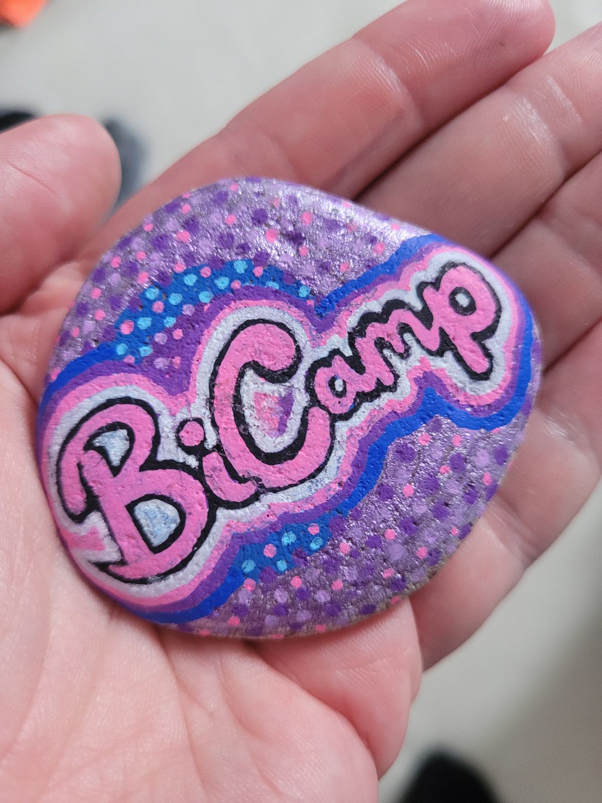 Photo of a rock, on which the word 'Bicamp' has been drawn in stylised script, with a halo of bright pinks, blues and purples surrounding it.