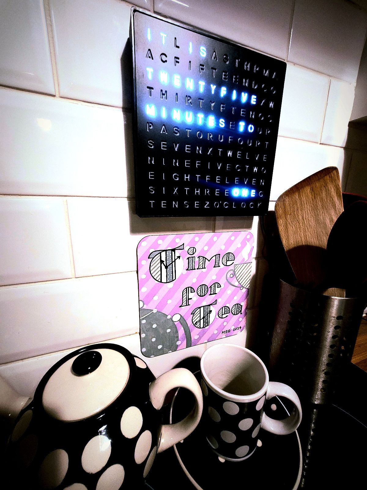 Copy of the 'Time for Tea' artwork in place underneath a clock in the artist's kitchen, with a teapot and mug below