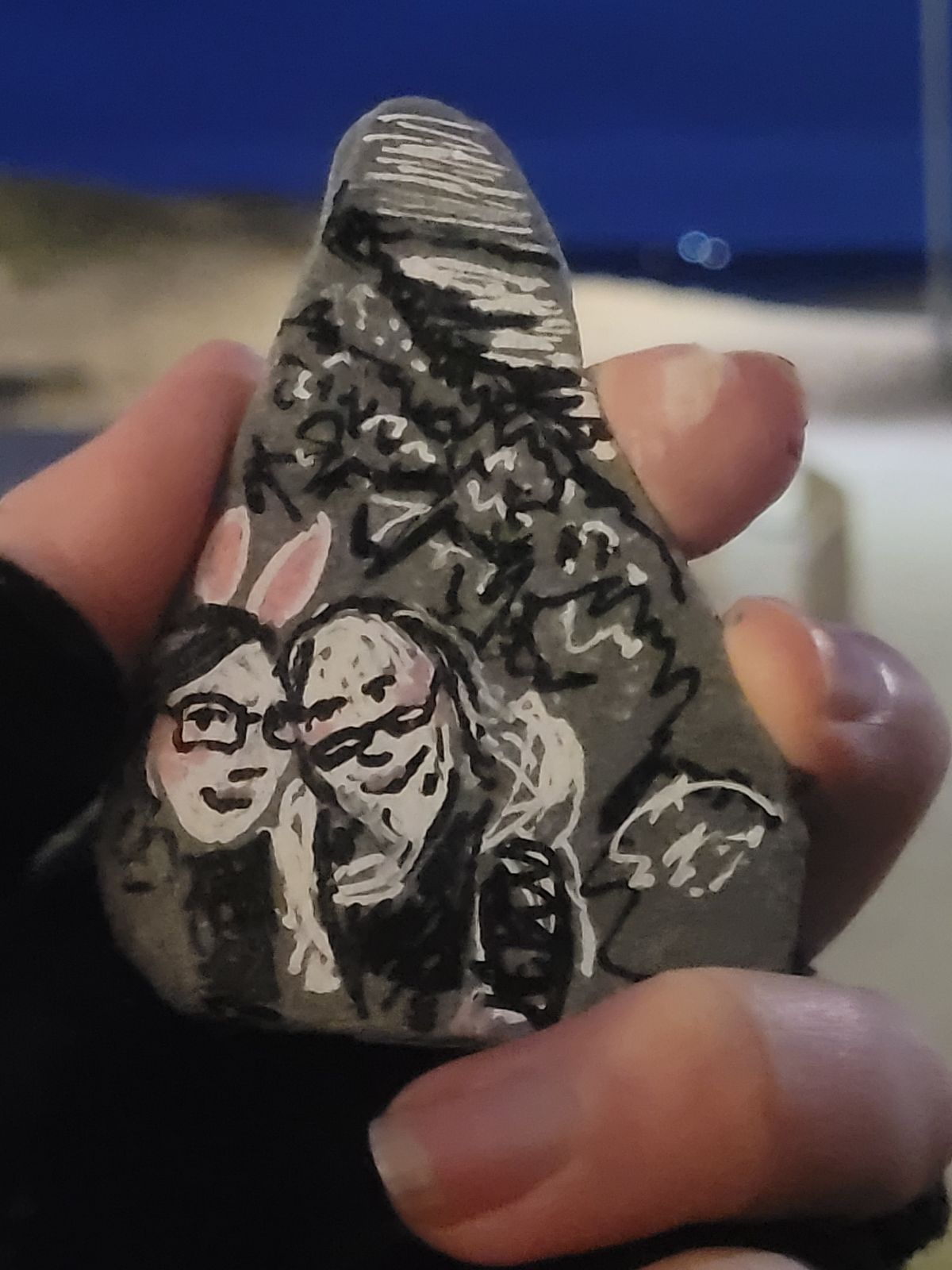 Photograph of a rock on which an image of the artist and their partner is painted. The artist is wearing white and pink bunny ears.