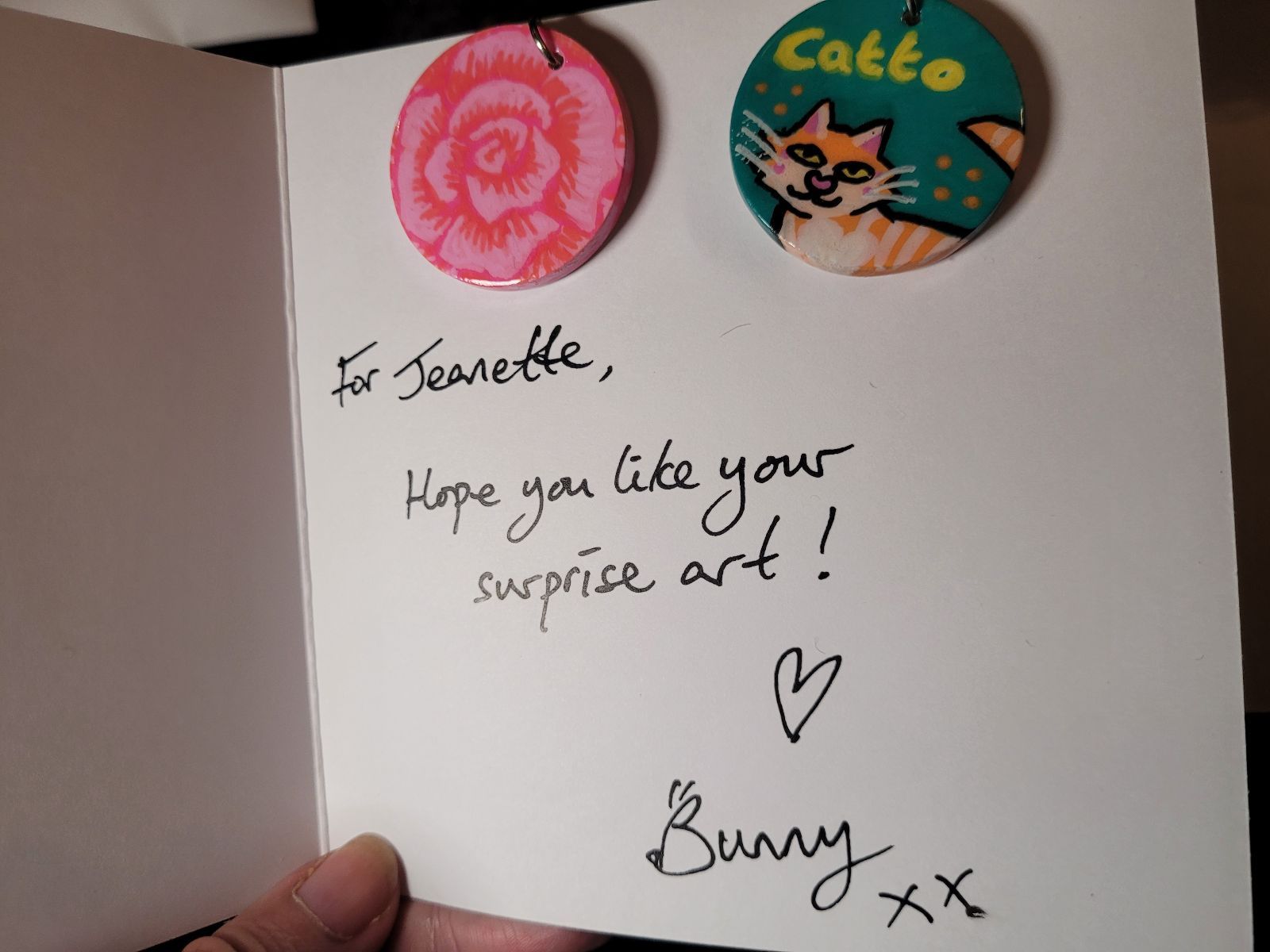 Card addressed to an art giveaway recipient, with two badges: a pink rose, and an orange catto.