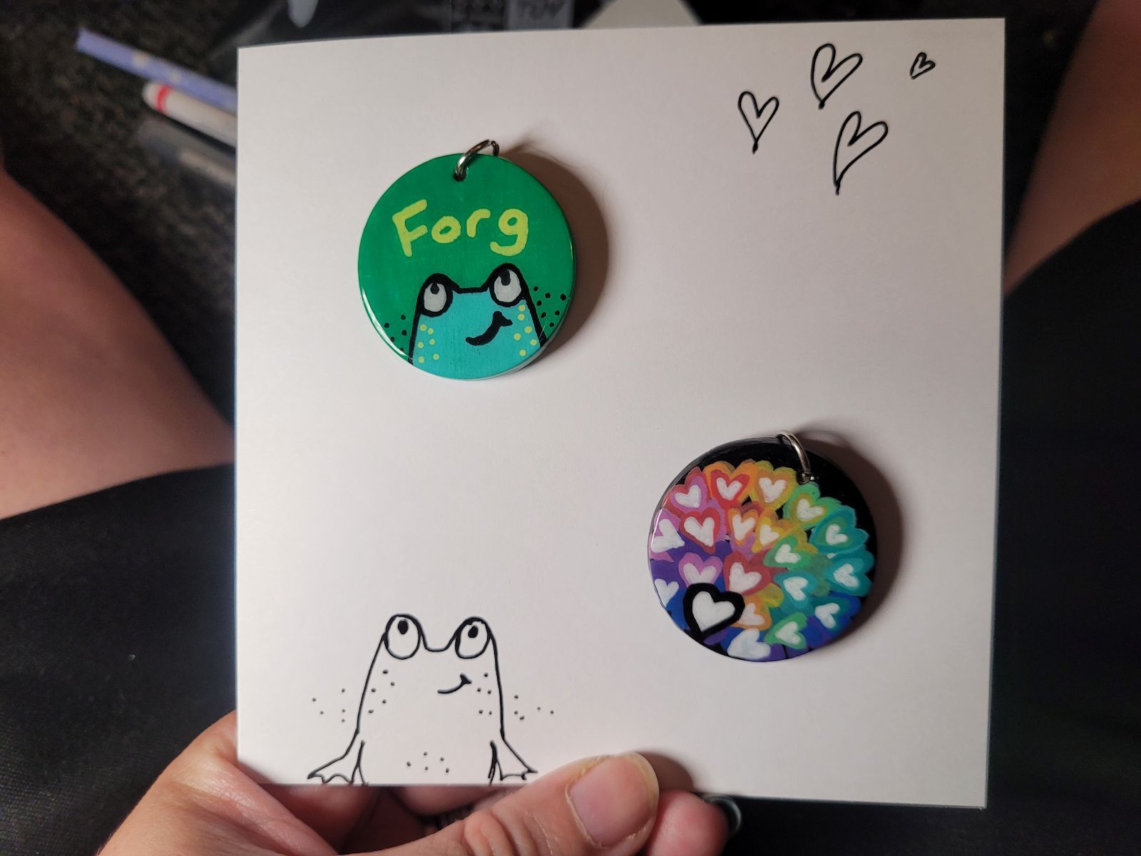 Two badges pinned to a hand drawn gift card with a frog sketched on it.