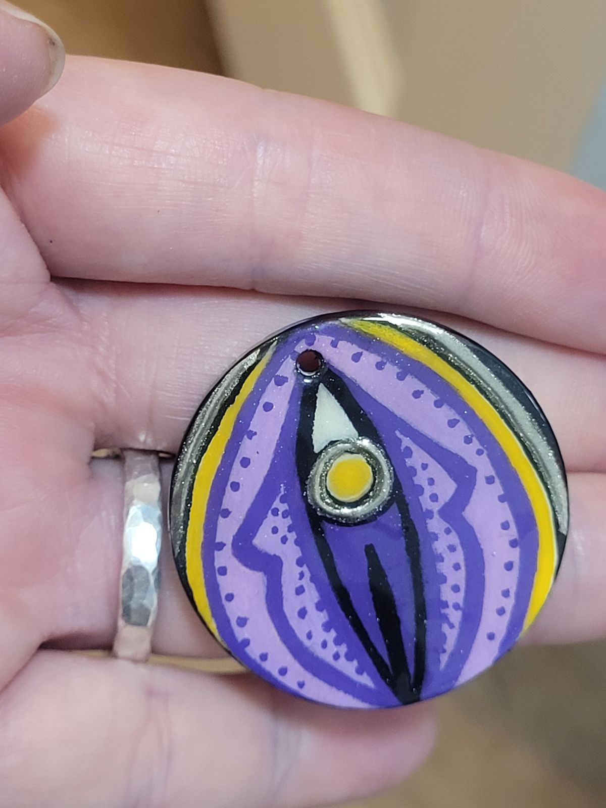 An abstract design reminiscent of a vulva, drawn in non-binary flag colours (black, white, yellow and purple). The 'clitoris' and a thin circle around the outer edge are gilded.