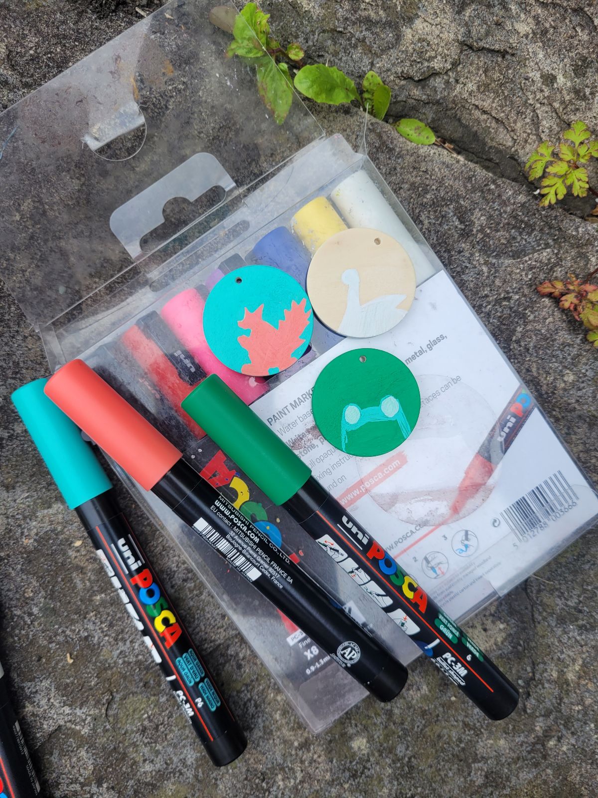 Photo of paint pens and in-progress badges taken outdoors on a stone background.