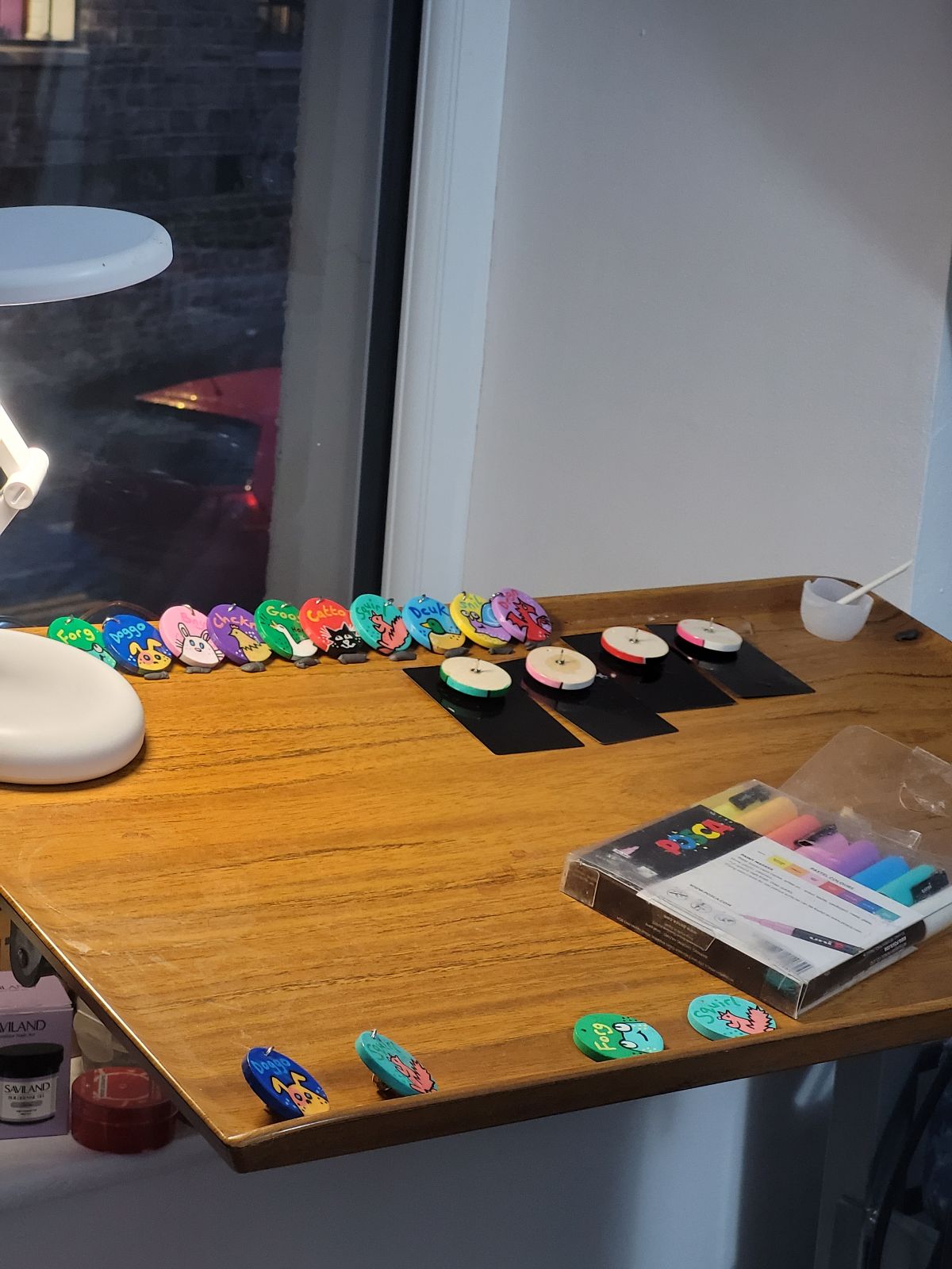 Close up photo of rolling desk with paint pens and in-progress badges.