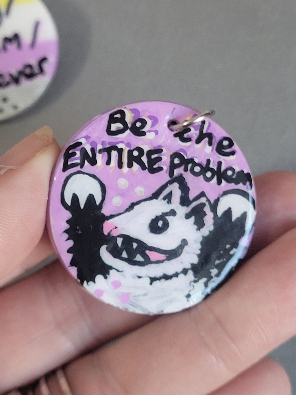 Badge with a cartoon possum on a lilac background that reads 'Be the ENTIRE problem'