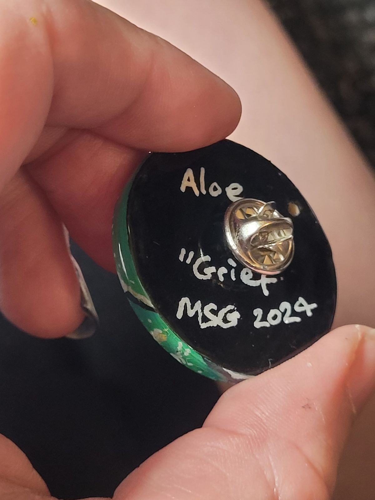 Reverse of aloe badge reads 'Aloe - Grief' and the artist's signature.