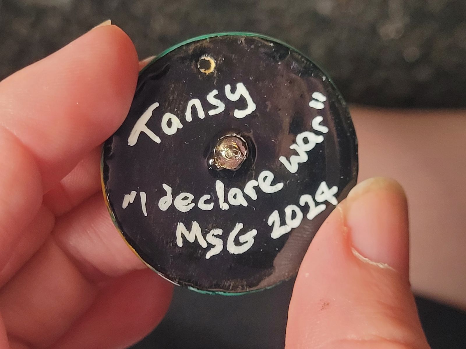 Reverse of tansy badge reads 'Tansy - I declare war', and the artist's signature.