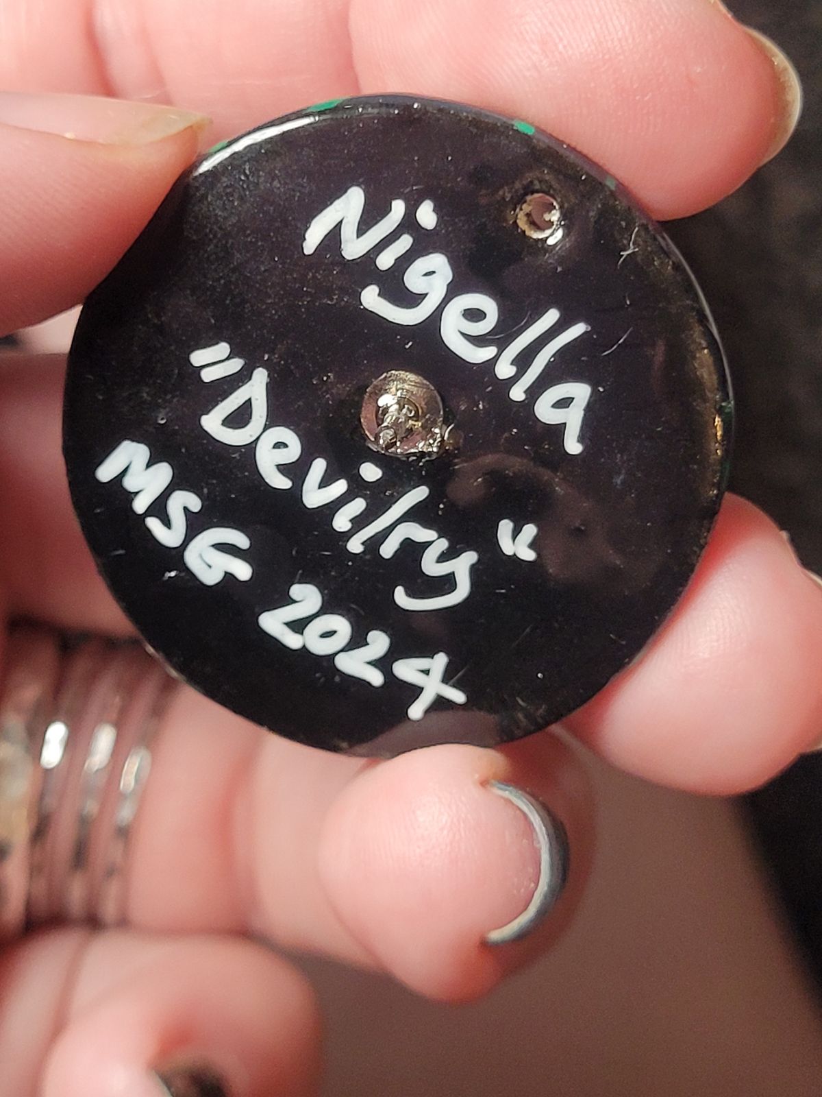 Reverse of nigella badge reads 'Nigella - Devilry', and the artist's signature.