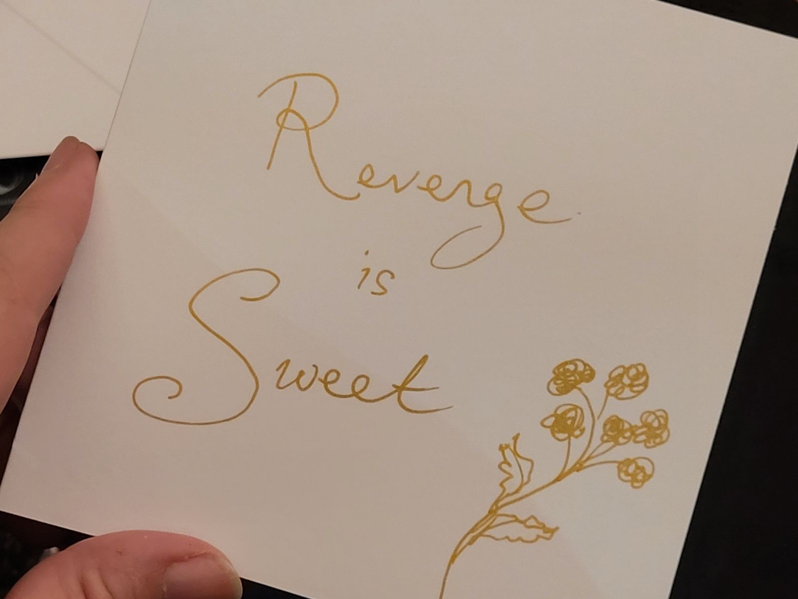 Gift card with 'Revenge is Sweet', and a sketch of tansy flowers drawn in gold pen.