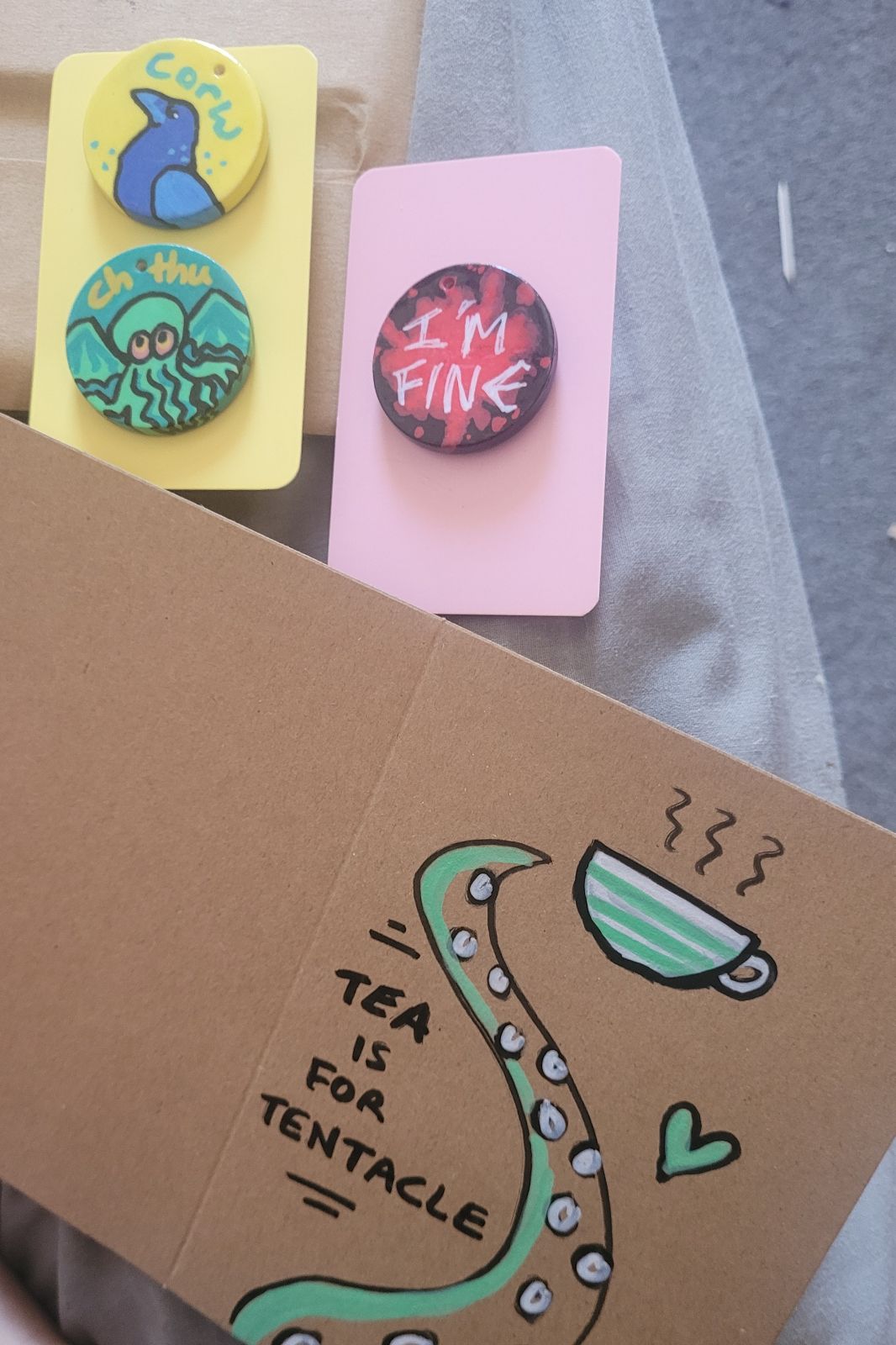 Crow and Cthulhu badges on gift cards ready to post out, with a hand drawn card reading 'tea is for tentacle'