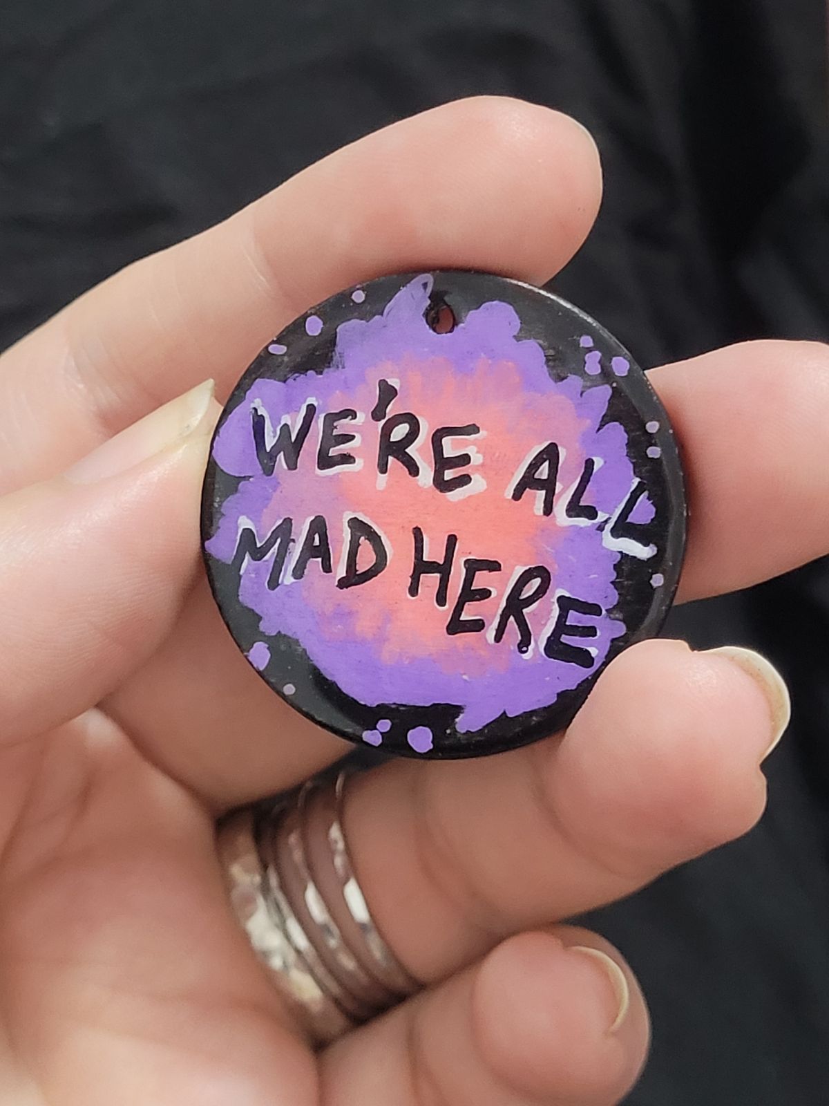 Purple and pink splatter effect badge: We're all mad here.