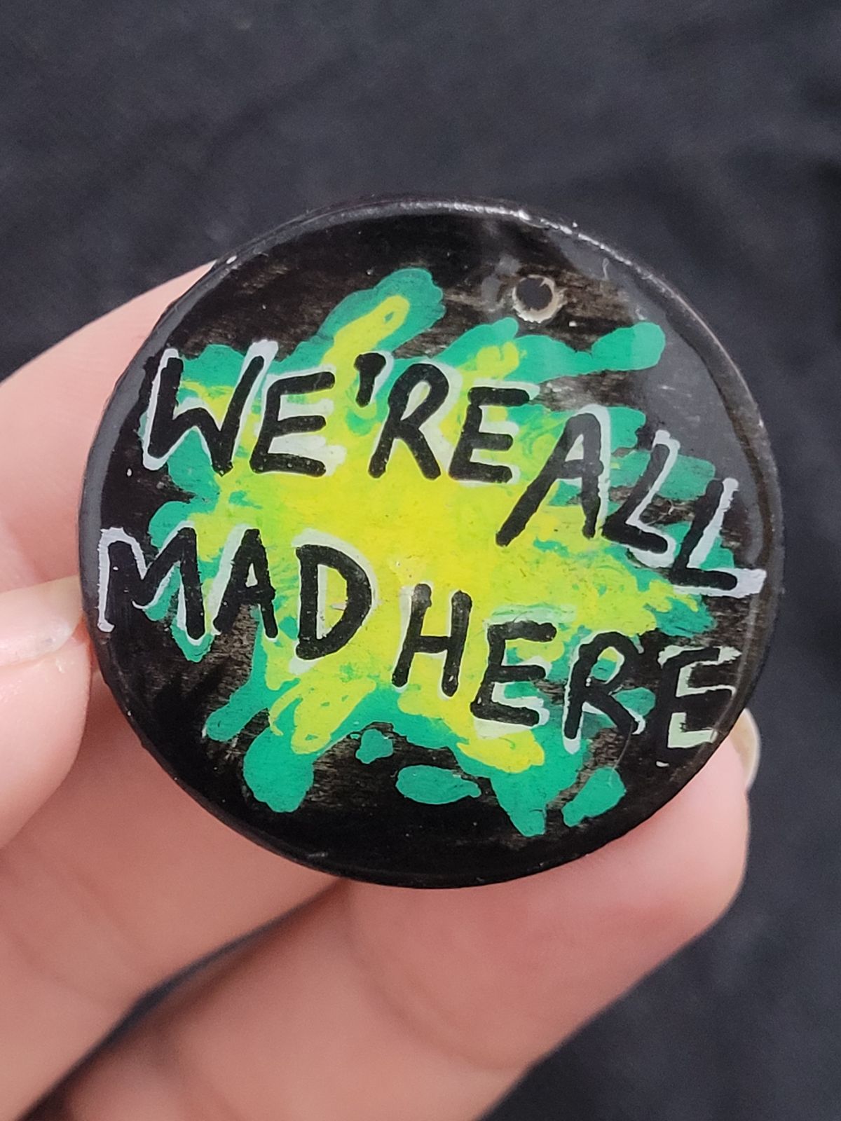 Green and yellow splatter effect badge: We're all mad here.