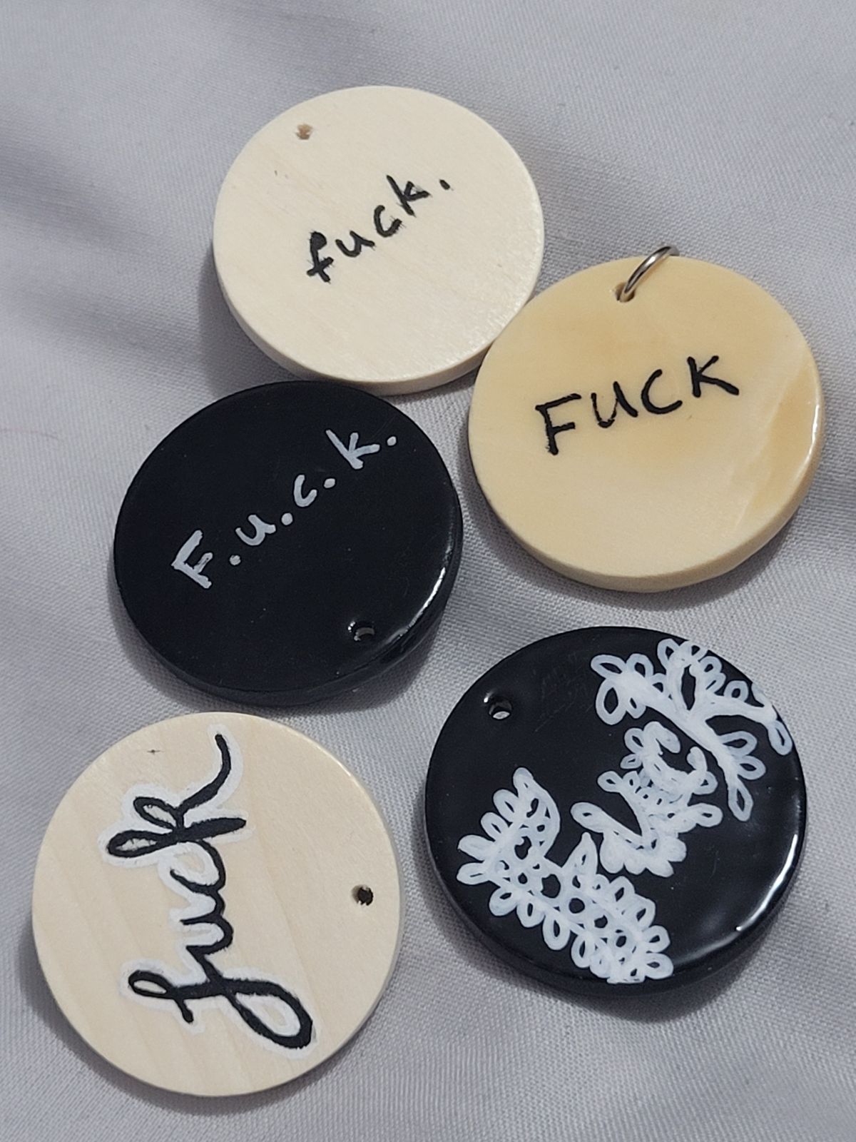 Five very simple black and white badges reading 'FUCK' in various styles of lettering.