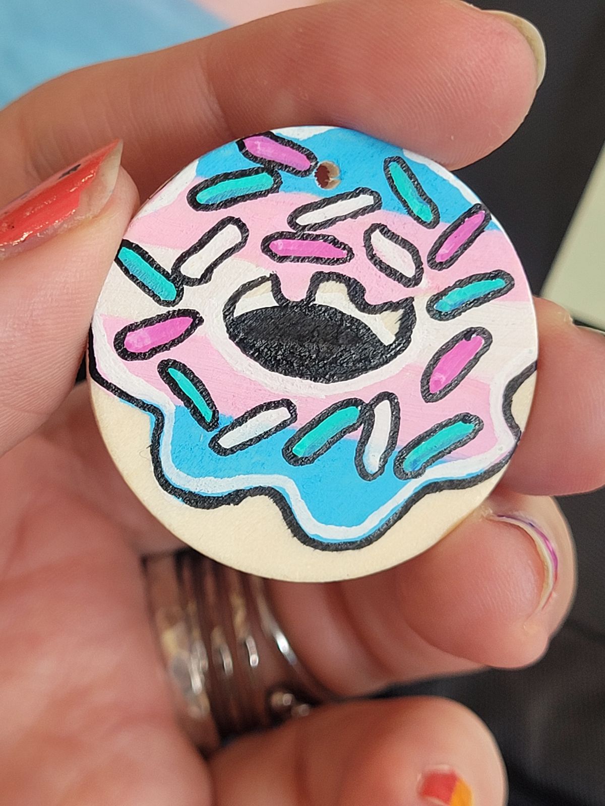 A badge made to look like a ring donut, with icing in the colours of the trans flag.