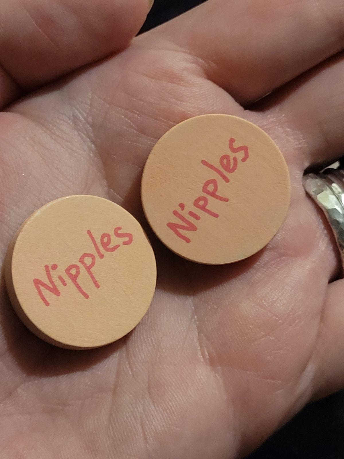 Badges with a beige background and the word 'Nipples' written across in a deeper pink tone.