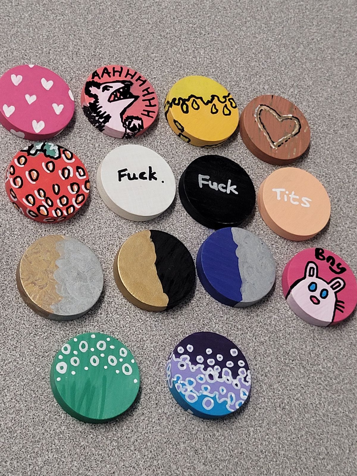 An array of brightly coloured badges, contrasted by two stark black and white 'fucks' and a white on beige 'tits' badge.