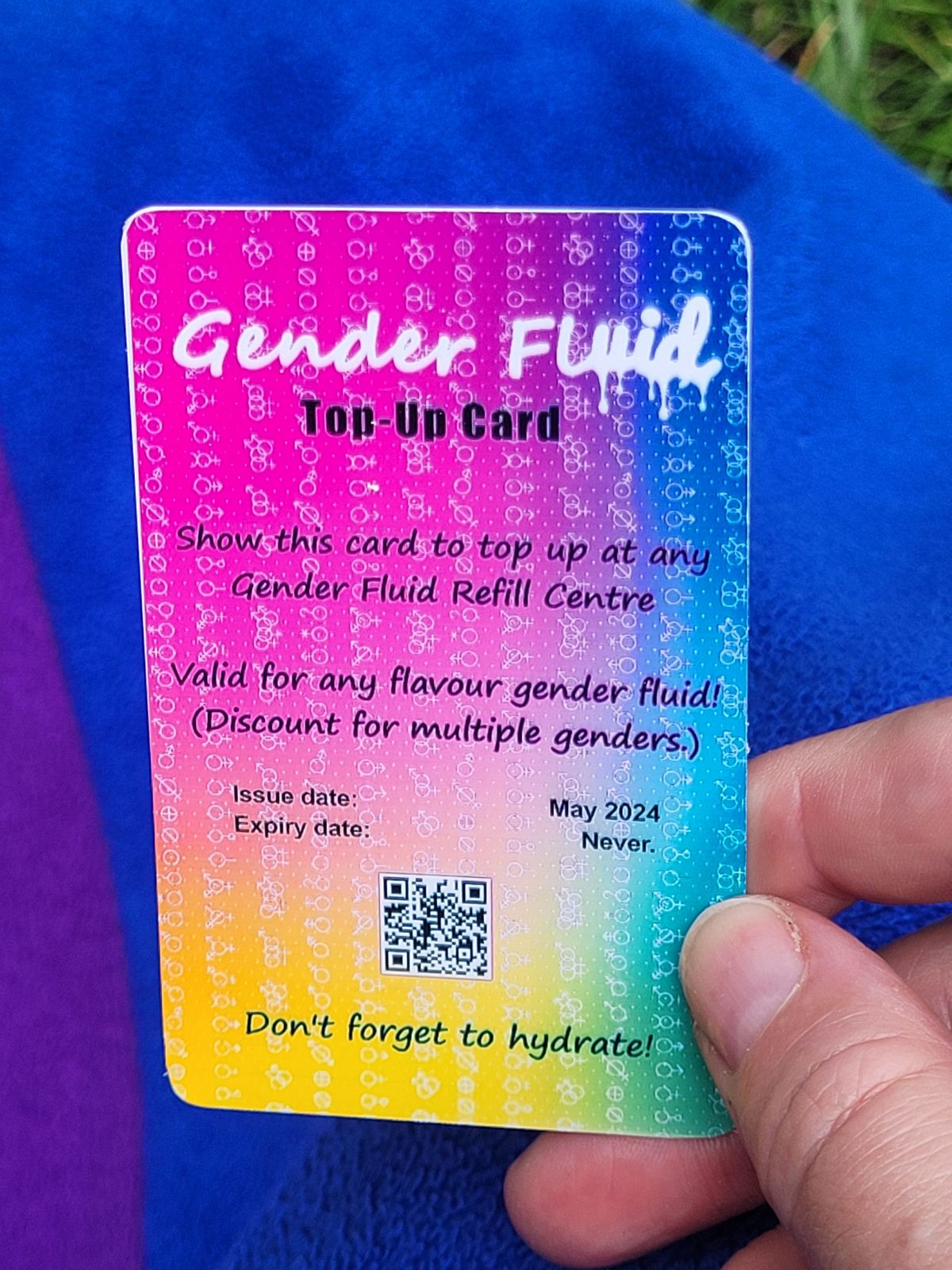 On a rainbow background, white text that looks like it is written in dripping paint reads 'Gender Fluid' with 'top- up card' written below. Show this card to top up at any Gender Fluid Refill Centre. Don't forget to hydrate!